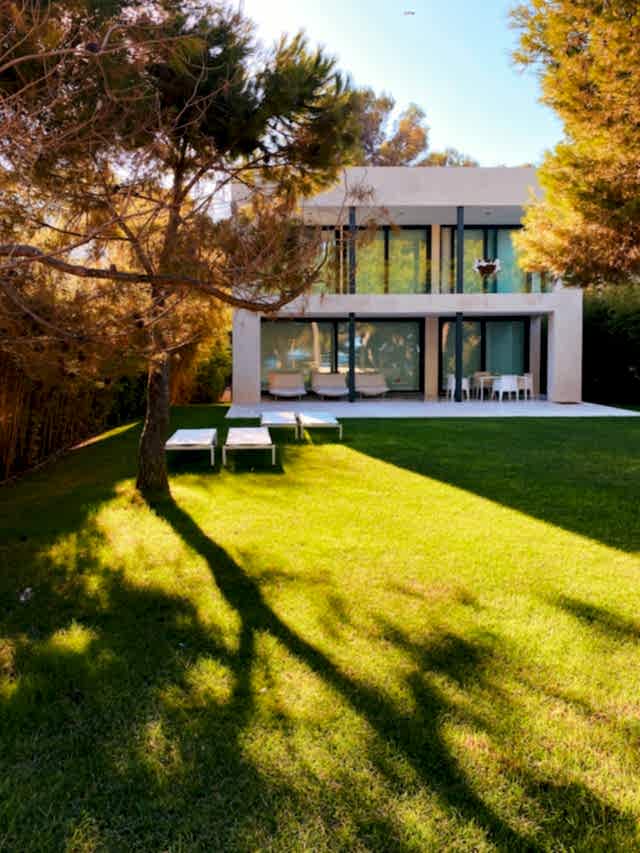 A sun-drenched, immaculate lawn in a modern backyard with white sun chairs.